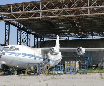 Verlassen steht eine Antonov An-12 vor einem ehemaligen Hangar. Beide rosten vor sich hin.