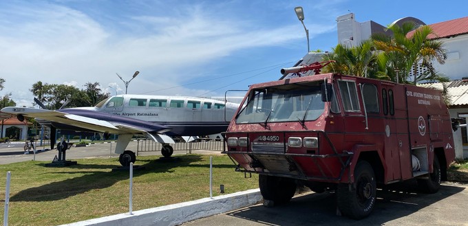 Ein historisches Feuerwehrfahrzeug und eine Cessna 404 Titan, die einst Inlandsrouten bediente, stehen dekorativ vor dem Airport.