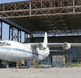 Verlassen steht eine Antonov An-12 vor einem ehemaligen Hangar. Beide rosten vor sich hin.