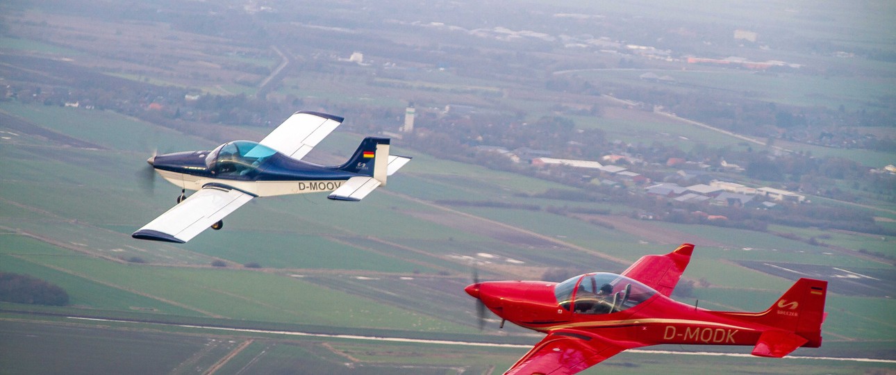 Zwei Breezer-Flugzeuge in der Luft: Das linke Flugzeug ist die erste Breezer aus dem Jahr 1999. Dahinter fliegt eine Breezer Sport.