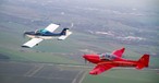 Zwei Breezer-Flugzeuge in der Luft: Das linke Flugzeug ist die erste Breezer aus dem Jahr 1999. Dahinter fliegt eine Breezer Sport.
