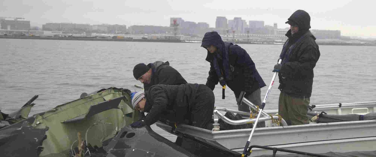 NTSB-Mitarbeiter an Wrackteilen im Potomac River: Untersuchung läuft.