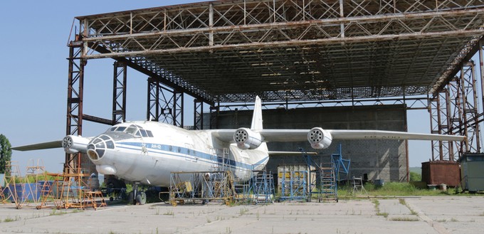 Verlassen steht eine Antonov An-12 vor einem ehemaligen Hangar. Beide rosten vor sich hin.