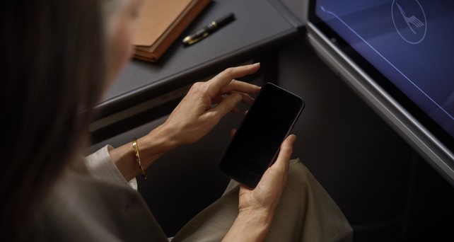 Lufthansa-Reisende hält ein Smartphone: Der Konzern wird alle 850 Flugzeuge mit Starlink ausstatten.