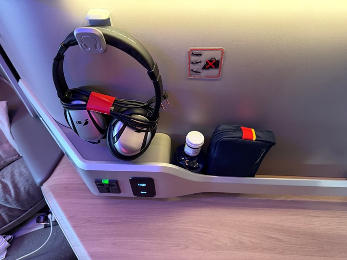 Links vom Sitz finden sich die Kopfhörer sowie eine große Ablagefläche mit einer Halterung für Bücher und mehr.