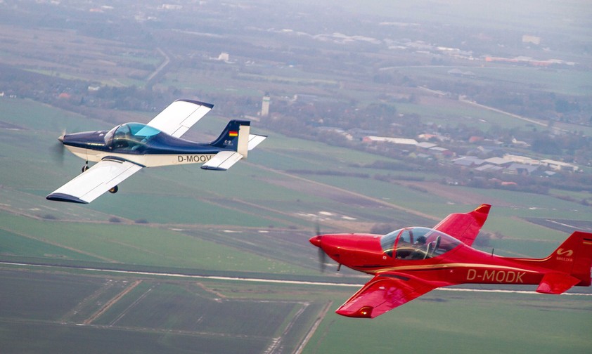 Zwei Breezer-Flugzeuge in der Luft: Das linke Flugzeug ist die erste Breezer aus dem Jahr 1999. Dahinter fliegt eine Breezer Sport.