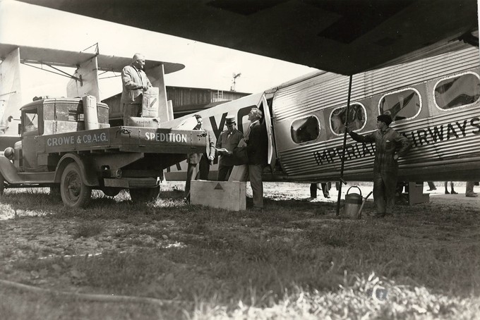 Ursprung der zivilen Linienflüge waren in den 1920er Jahren weniger die Passagierdienste als die rasche und zuverlässige Auslieferung von Post und Frachtpapieren, also Dienste, die heute durch die Integrators geleistet werden. Die Spedition Crowe &amp; Co. A.G. hat Luftfracht nach England angeliefert. Vor dem Verladen der Fracht in die Heracles prüft der Zollbeamte intensiv die Papiere.