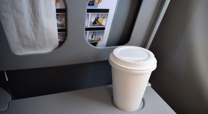 Kaffeebecher auf einem Flugzeugklapptisch: Einige Airlines verbieten jetzt das mitgebrachte Heißgetränk.