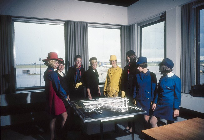 Uniformen-Parade: Flugbegleiterinnen von Germanair, Bavaria, Pan Am, Lufthansa und BEA schauen sich das Modell eines geplanten Flughafengebäudes an.