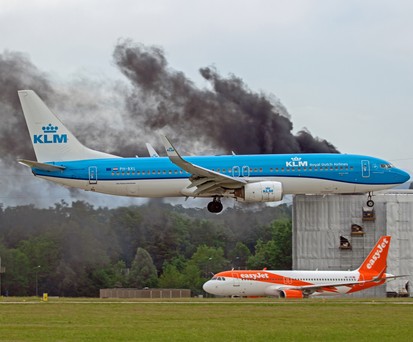 Eine Maschine von KLM fliegt am brennenden Gebäude ...