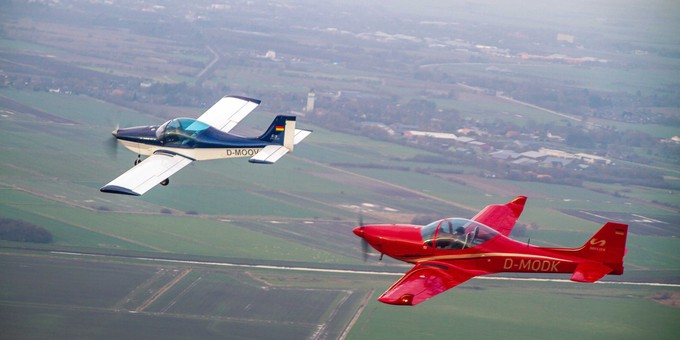 Zwei Breezer-Flugzeuge in der Luft: Das linke Flugzeug ist die erste Breezer aus dem Jahr 1999. Dahinter fliegt eine Breezer Sport.